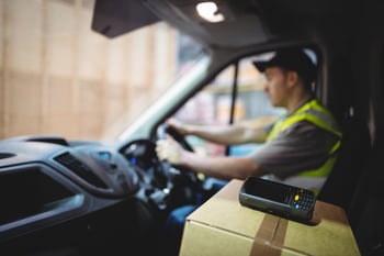 Delivery driver driving van with parcels on seat outside warehouse