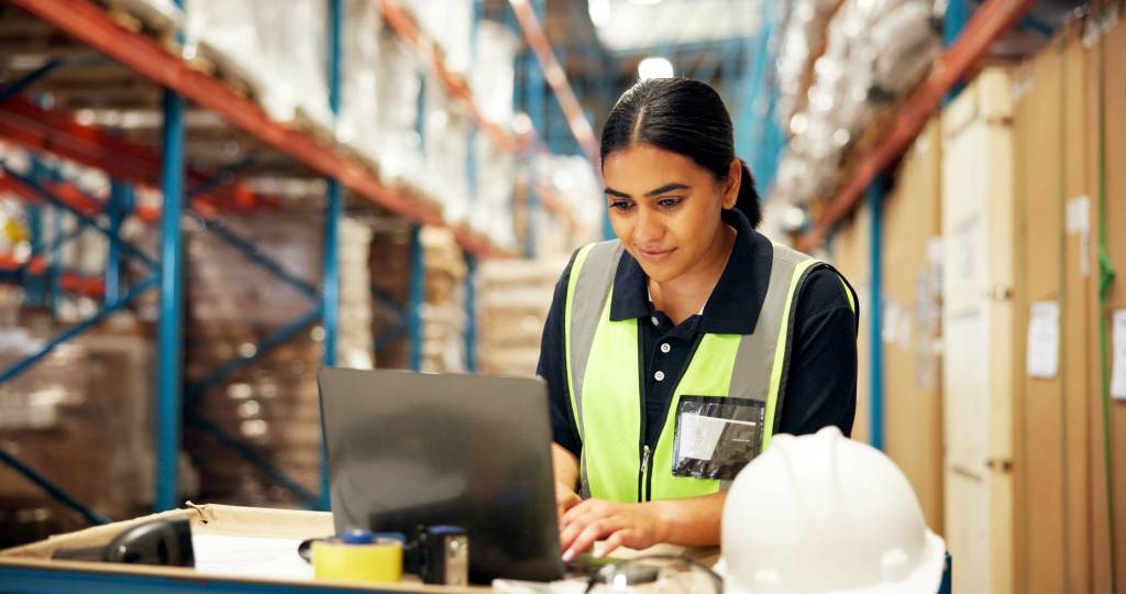 Woman typing on a laptop in a warehouse