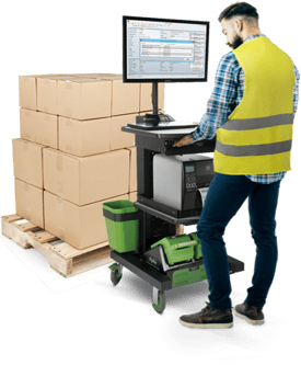 A warehouse worker using a mobile workstation with a pallet of stacked boxes nearby.